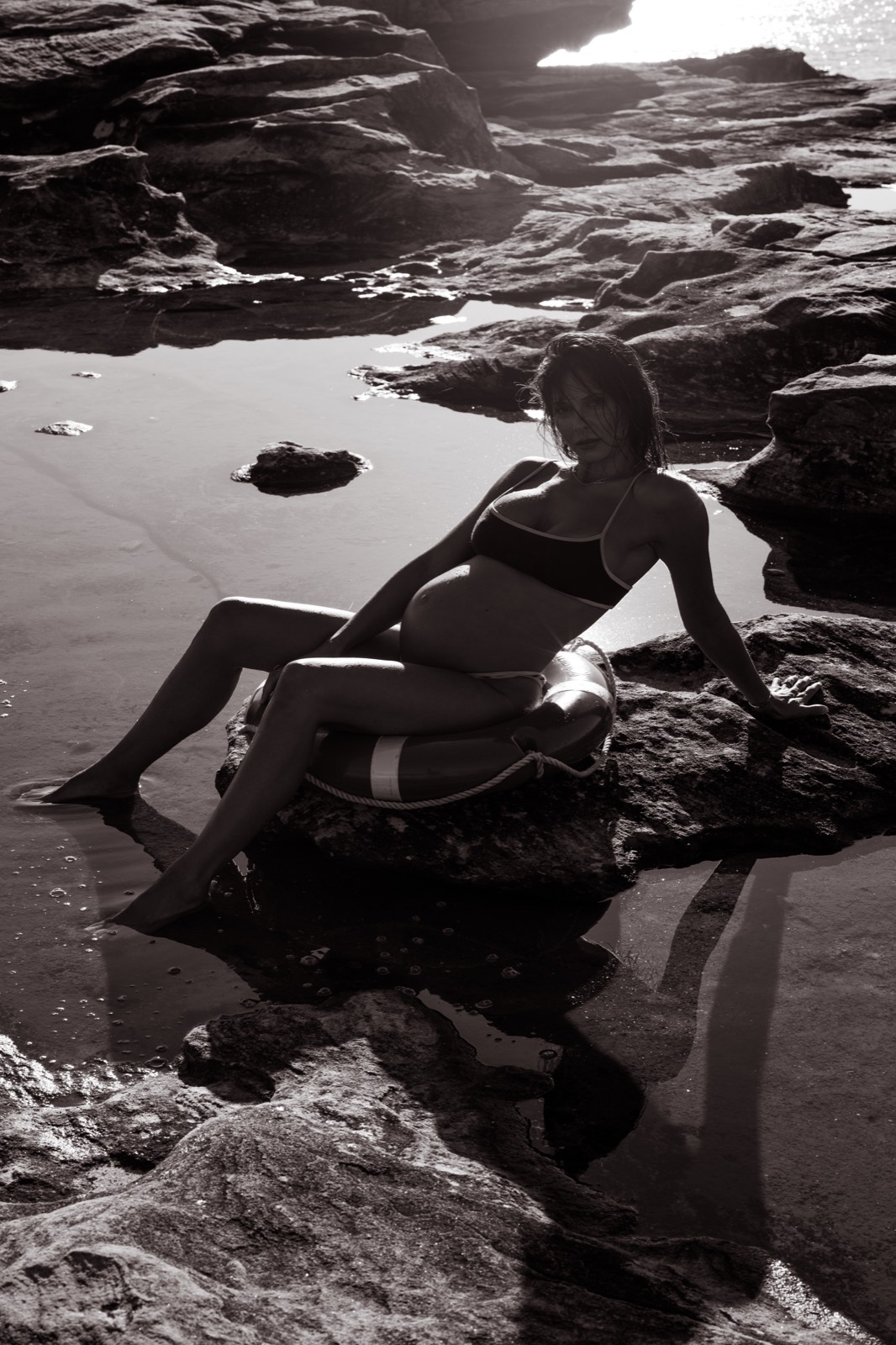 Pregnant woman seated in a lifesaver ring on coastal rocks