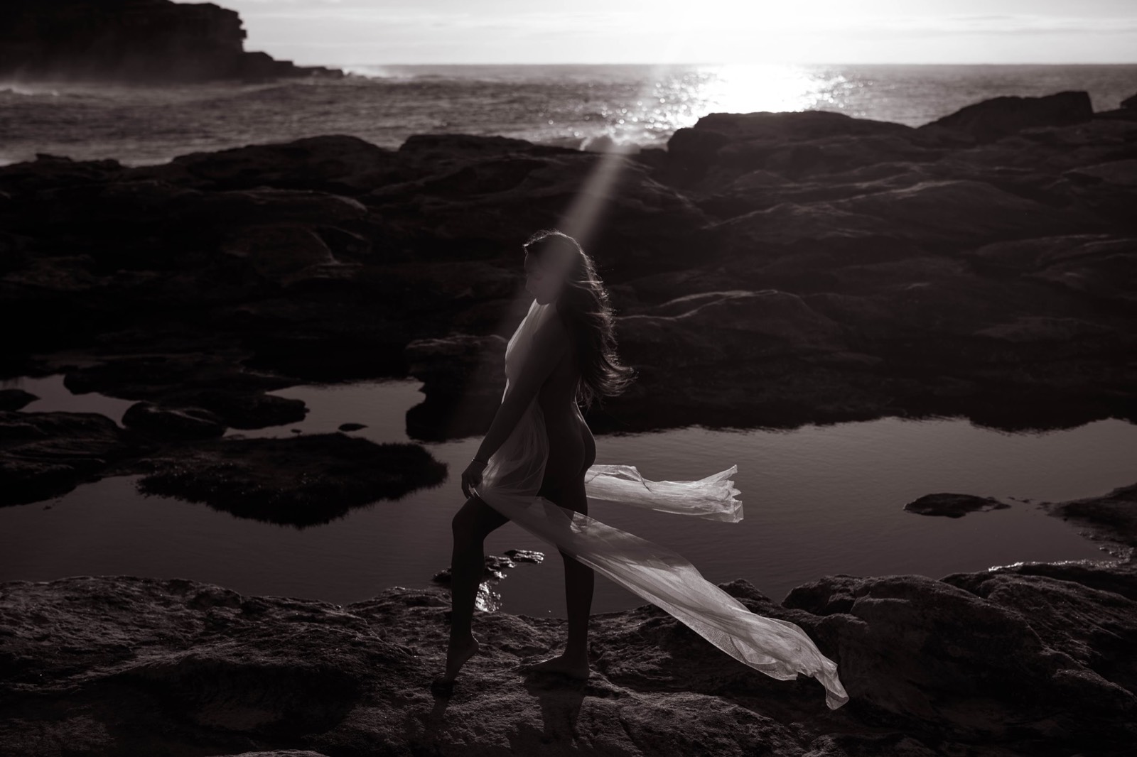 Panoramic black and white maternity portrait crossing coastal rocks