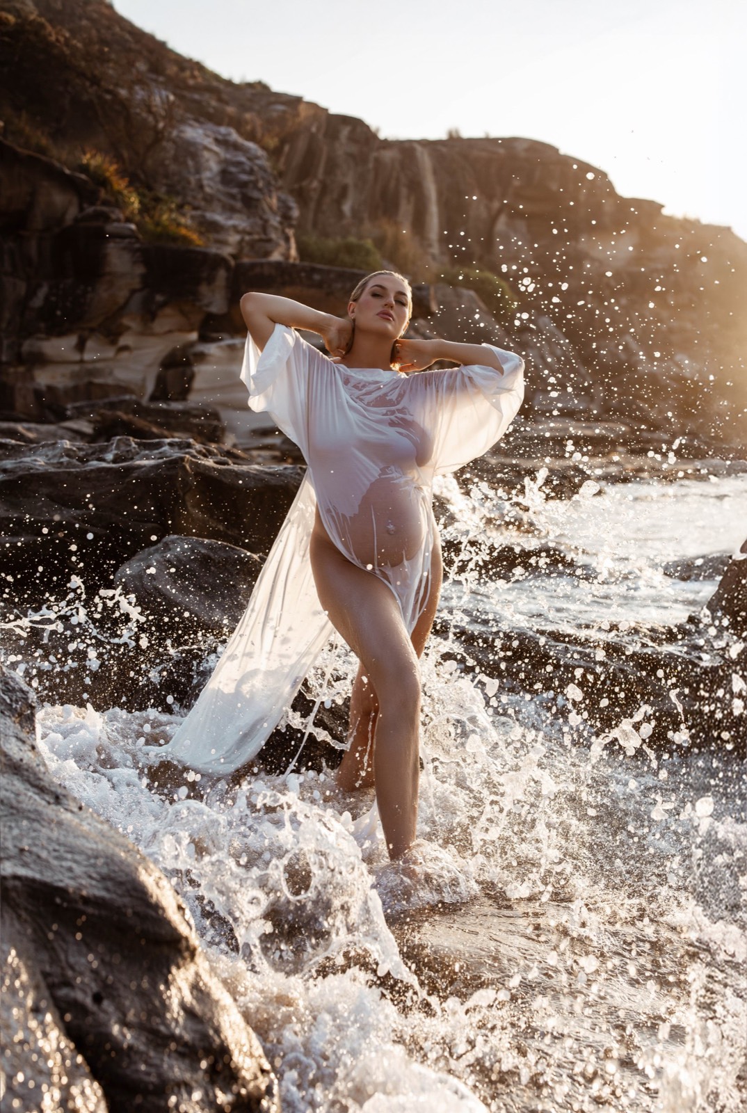 Maternity portrait standing in sunlit ocean spray