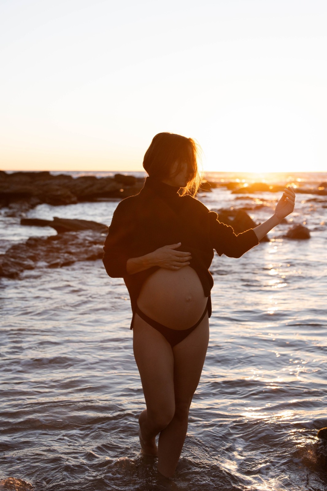 Golden silhouette of a pregnant woman moving through the sea