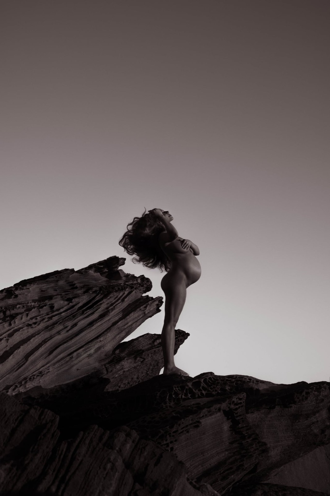 Sculptural black and white maternity silhouette on coastal rock