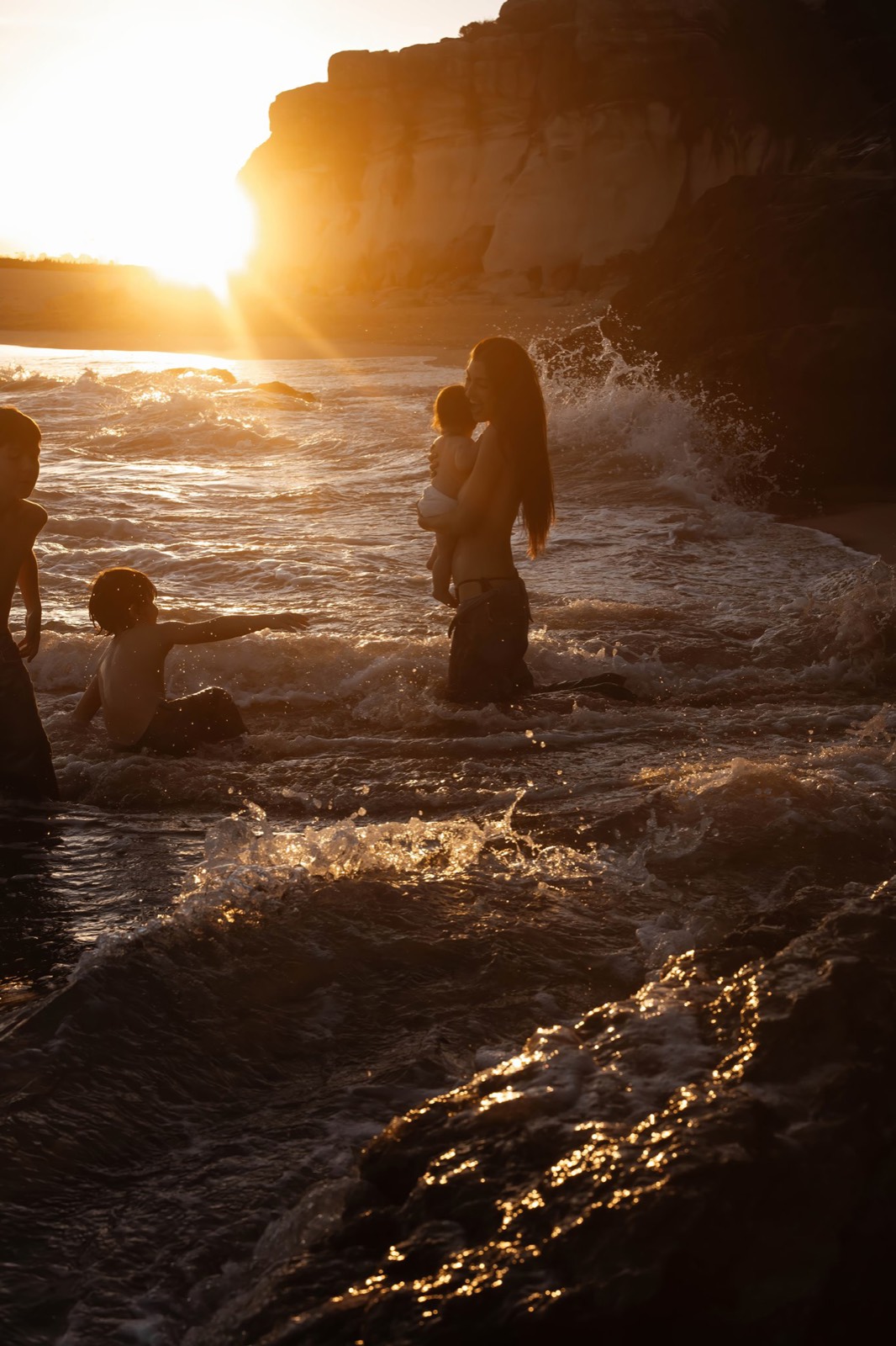 Mother with her children in the sea at sunset