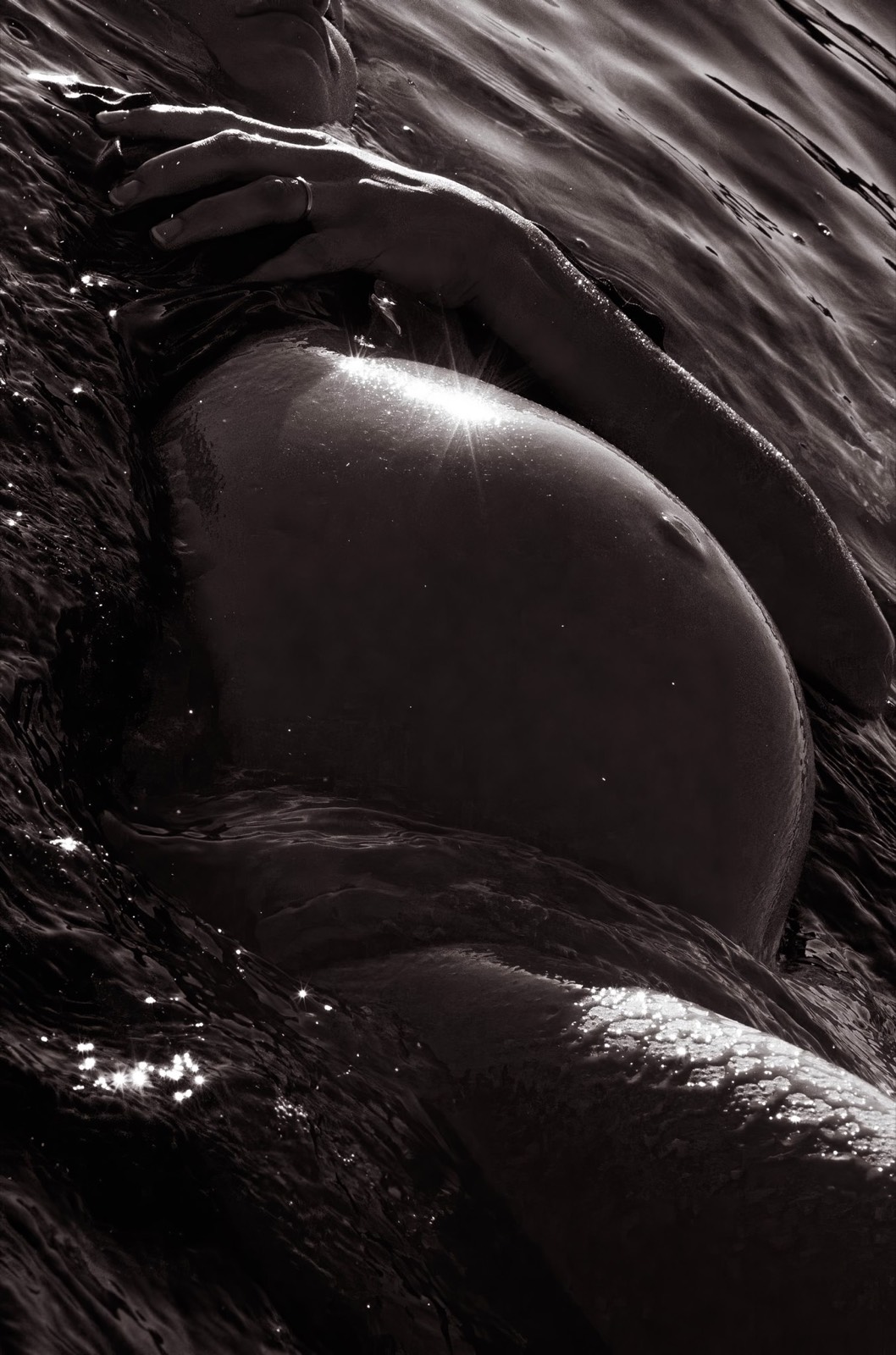 Intimate study of hands resting across a sunlit pregnant belly