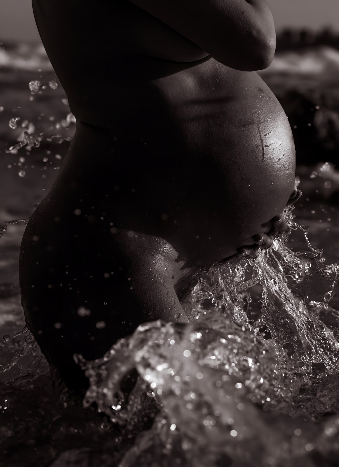Black and white maternity study holding the belly in ocean spray