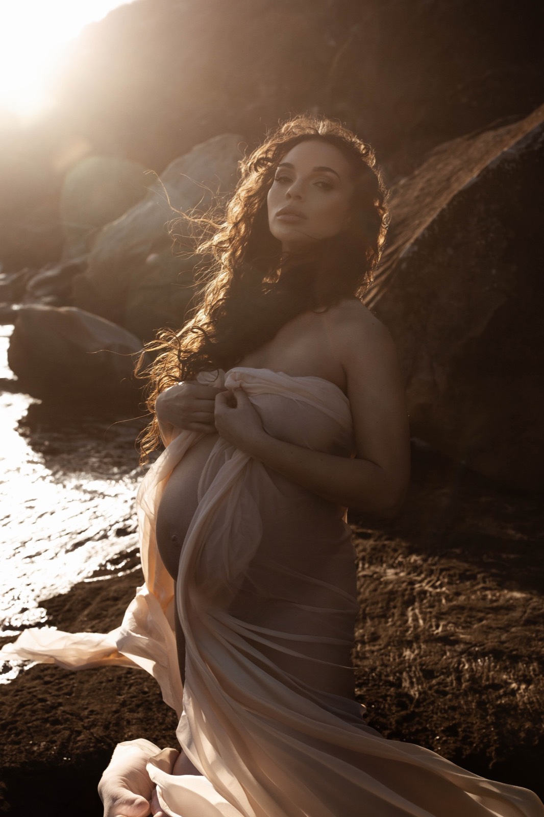 Golden-hour maternity portrait wrapped in translucent fabric